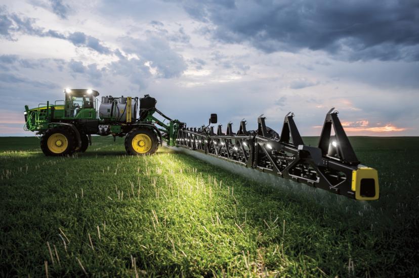 A green John Deere tractor spraying a field at dusk