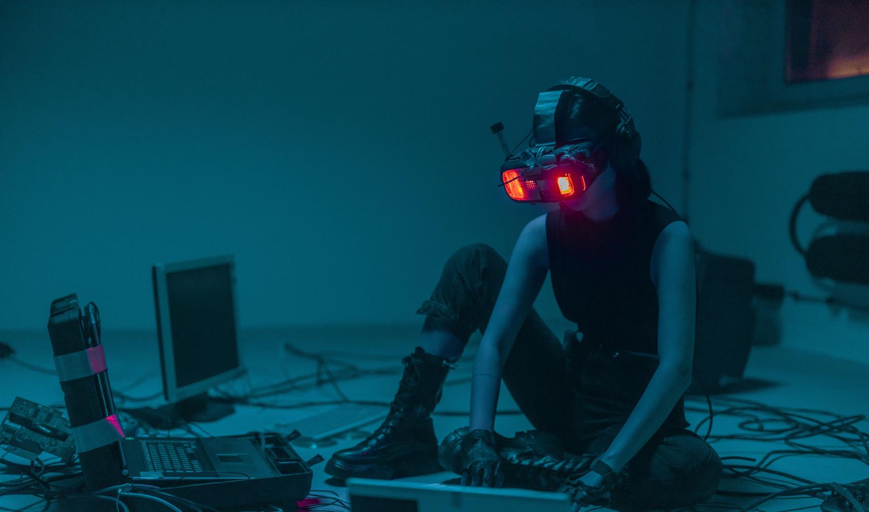 Person sat on floor using spatial computing headset and keyboard surrounded by other technology detritus