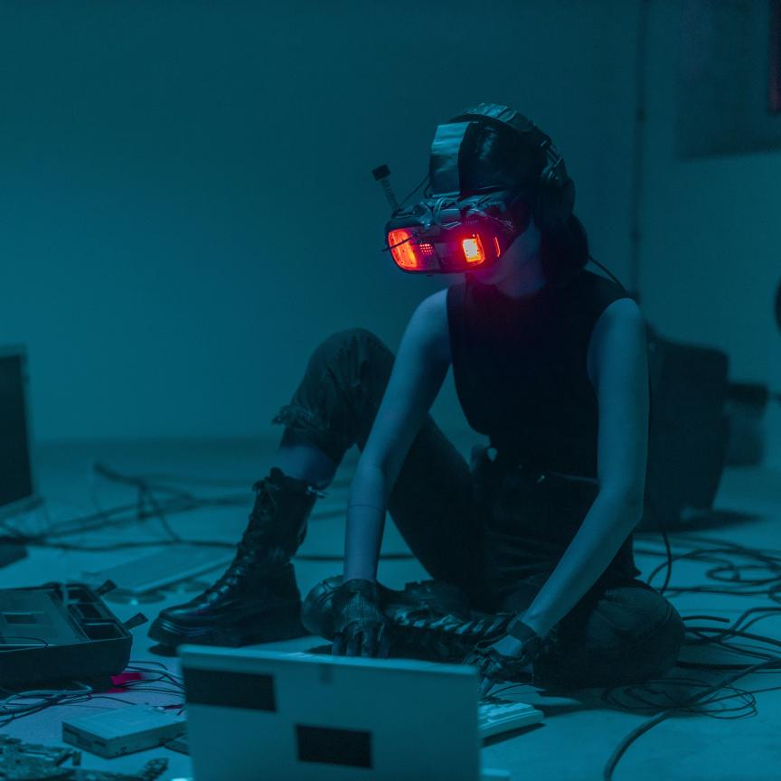 Person sat on floor using spatial computing headset and keyboard surrounded by other technology detritus